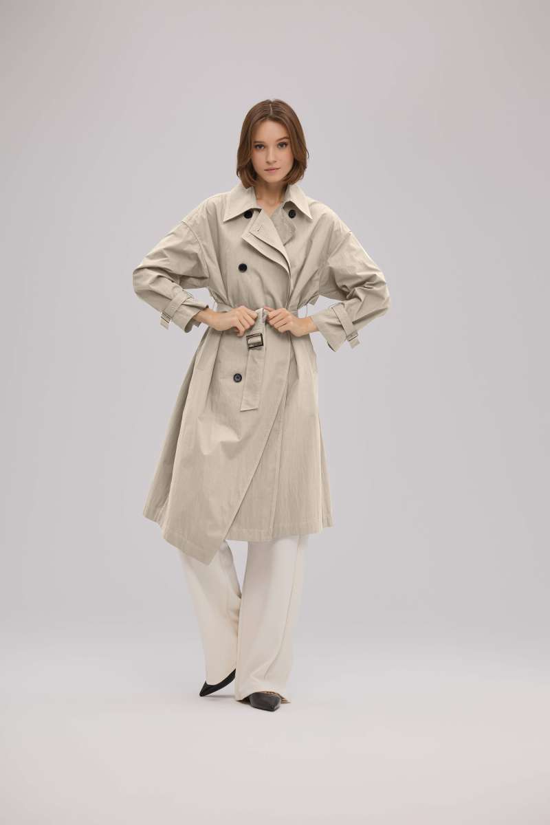 Model in beigem Trenchcoat und weiter cremefarbener Hose aus dem sego Sortiment